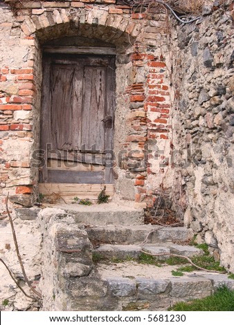 An old, rotten door in a brick wall with stairs in front