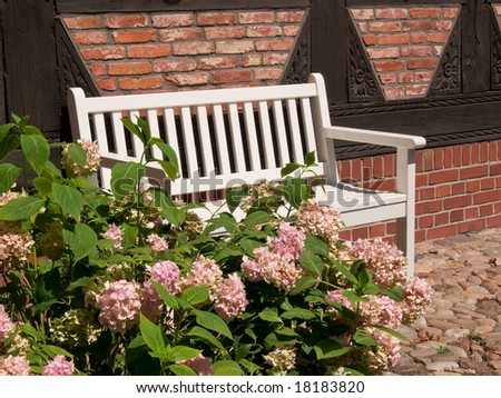 White bench with pink flowers in front of a half-timbered house