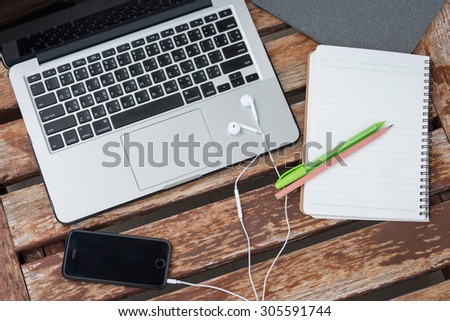 Open laptop with cell phone, headphones, note and pen on the old wooden table.
