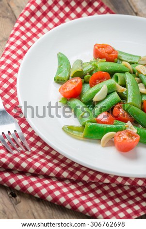 Stir fry sugar snap peas with tomato on white dish.