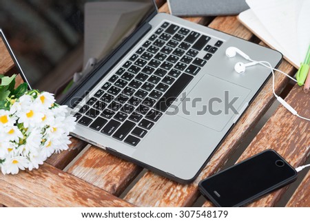 Open laptop with cell phone, headphones and note on the old wooden table.