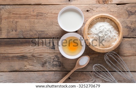 The flour in a wooden bowl, egg, milk and whip for beating.