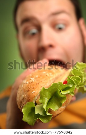 funny guy eating hamburger on green background (focus on salad)
