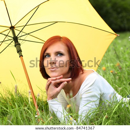 beautiful girl relaxing on grass under yellow umbrella
