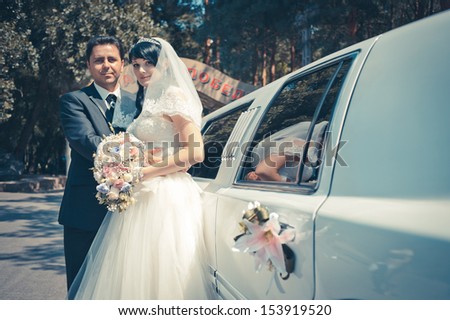 bride and groom near the limousine with wedding bouquet