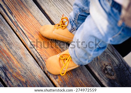 baby feet in fashionable jeans and shoes on the bench