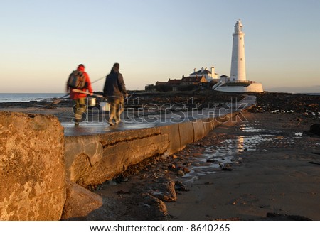 Fishing men walking to St Mary\'s Lighthouse early morning with the tide out exposing causeway to island