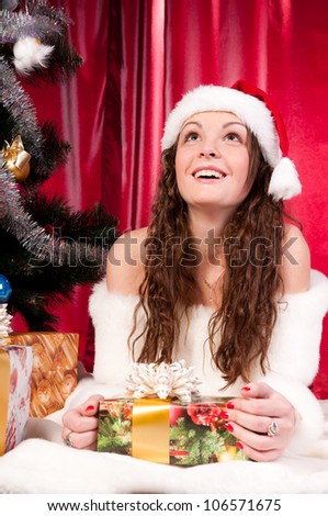 Girl gets a Christmas gift, decorated Christmas tree, red background, beautiful clothes