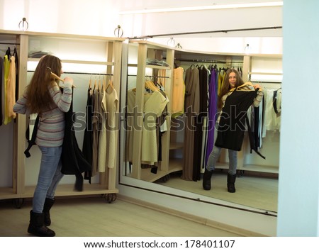Woman shopping choosing dresses looking in mirror uncertain. Beautiful young multicultural shopper in clothing store.
