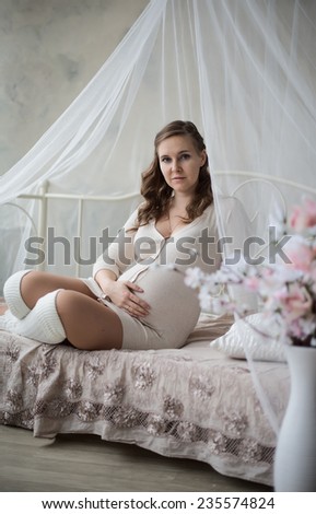 Pregnancy, motherhood and happy future mother concept - pregnant woman and bouquet flowers sitting on the bed