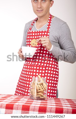 Portrait of a young attractive male cook drinking coffee and eating cookies.