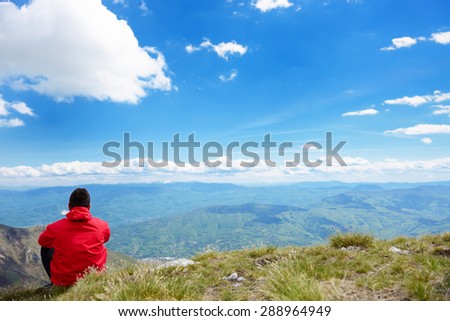The young man sits on top of the mountain, in front of it is a beautiful landscape