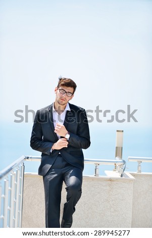 Businessman standing at the balcony near sea under blue sky