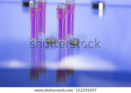 Four plastic tubes filled with pink fluid in a blue lit room laboratory/Laboratory samples