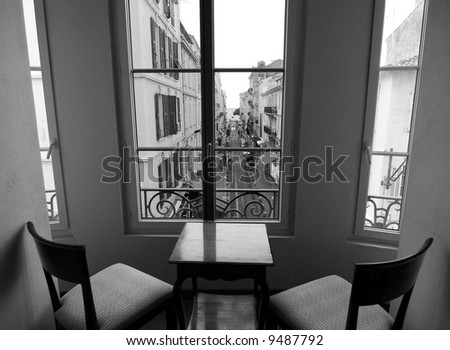 Black and white image of a street of Cannes seen from a room with two chairs and a table