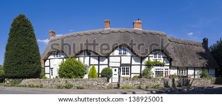 Pretty country village scenic of traditional thatched cottages and pristine gardens. Stitched panoramic image.