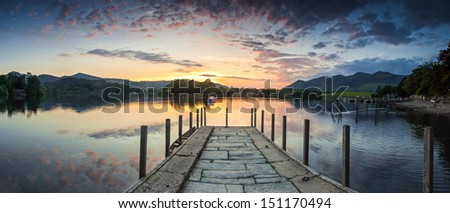 Inviting Jetty Leading To A Dramatic Sunset Reflected In A Perfectly Still Derwent Water, Lake District, Uk.