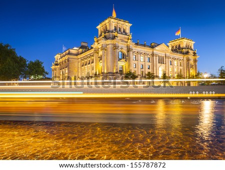 Motion blurred cruise boat passes in front of the mighty Reichstag parliament (1894) illuminated at night and reflected in the river Spree, Berlin, Germany.
