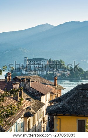San Giulio island, sun dappled villas and misty mountains at lake Orta in Italy.