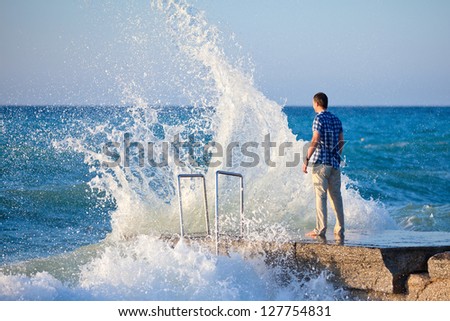 Young man on the pier and big wave with splashes