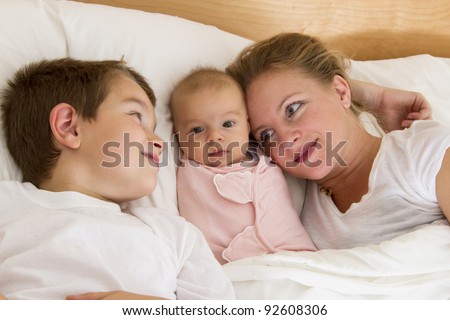 Mother and her kids in the bed, big brother looking his mother while newborn swaddled between them.