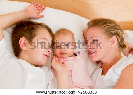 Mother and her kids in the bed, big brother and mother looking at  newborn swaddled newborn.