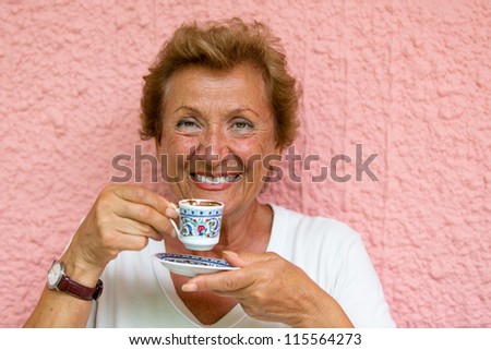 Older Lady drinking her Turkish coffee infront of pink  textured wall