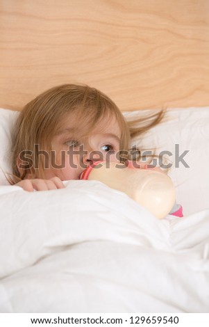 Cute toddler getting nutritious milk before goes to sleep under the blanket.