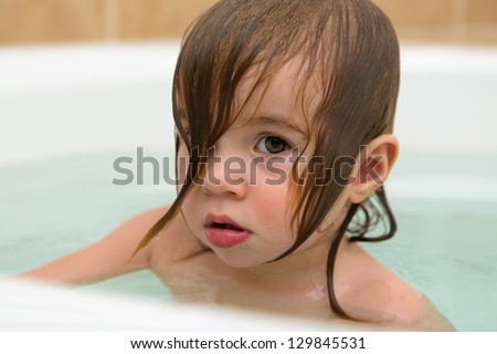 Big eye toddler girl giving thoughtful expression, perhaps attitude. She has wet hair in the bath tub.