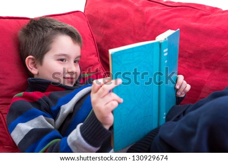 Kid enjoy reading the novel on the comfortable red couch.