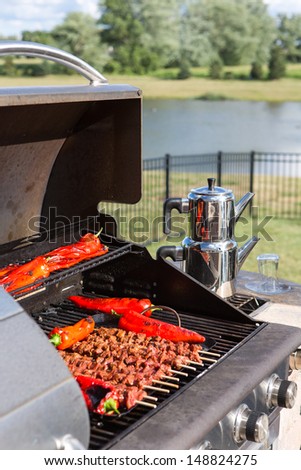 Barbecuing Skewers and red chilies outside. Turkish tea kettle on the side burner next to the BBQ.