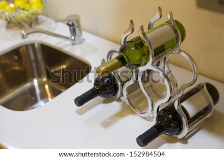 Three bottles of wine with blank labels in a stylish wine rack on a kitchen or bar counter alongside a sink