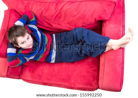 Young boy in his comfort zone, laying down on the red couch comfortably bare foot