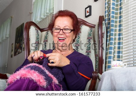 Senior happy woman laughing while knitting, she sits on a fancy old classic style chair