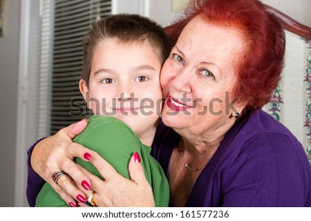 Grandmother's Love to her eight years old grandson, she hugs him tightly with a cheek to cheek touch while looking at you