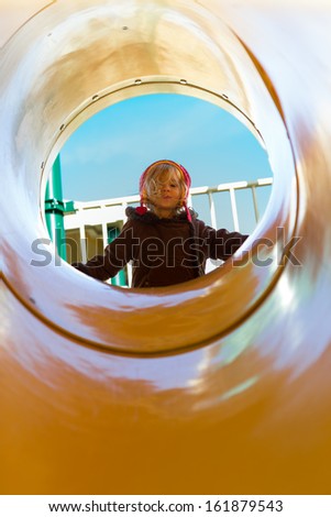 It\'s a sunny winter day at the other side of the yellow tube slide. Mischievous girl looking down from top of the slide with her coat perhaps getting ready to slide down.