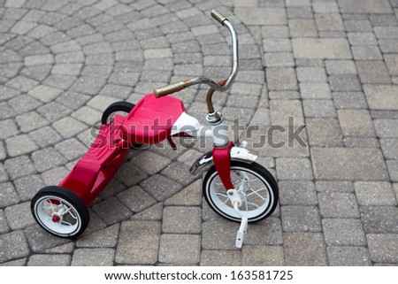 Child\'s red tricycle parked on a cobble design paved street