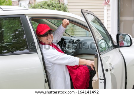 Senior lady with red hat sitting on the passenger seat getting ready close the door and hit the road, she has genuine smile on her face