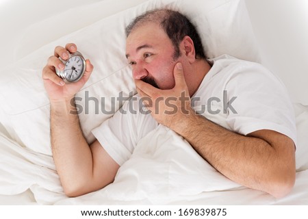 Man suffering from insomnia trying to sleep checking the time on his alarm clock in desperation as he realizes he will not wake up in time for work if he sleeps now