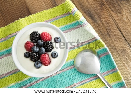 Delicious yogurt and fresh berries for breakfast with strawberries, blackberries and blueberries served on a colourful striped placemat