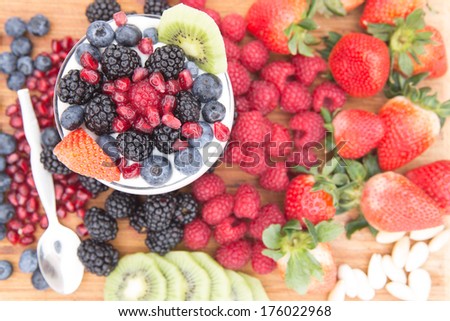 Healthy nutritious snack made of a bowl of raspberries, blackberries, blueberries, pomegranate, strawberries and kiwi, surrounded by fresh fruits on a wooden table