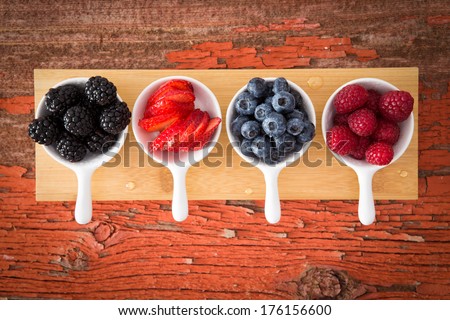 Fresh assorted berries on a grungy wooden counter displayed in small ceramic ramekins including blackberries, blueberries, strawberries and raspberries for a healthy snack or appetizer