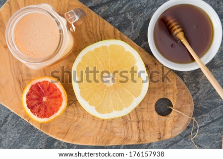 Freshly squeezed grapefruit juice served with a container of honey and two halved grapefruit on an old olive wood chopping board for a healthy breakfast, overhead view