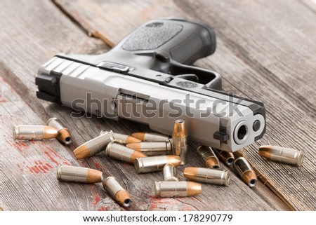 Close up view of the barrel of a handgun with scattered bullets and cartridges lying on old rustic wooden boards depicting violence, crime and robbery with copyspace