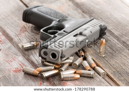 Looking up the muzzle of a handgun surrounded by scattered bullets and ammunition lying on old rustic wooden boards conceptual of violence, killing, crime and burglary