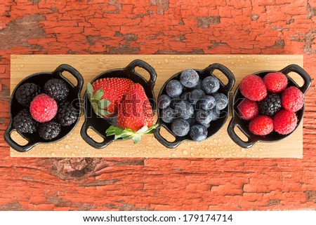 Assortment of ripe fresh autumn berries displayed on a wooden board in individual dishes with raspberries, blackberries, blueberries and raspberries on a grungy wooden table with peeling paint
