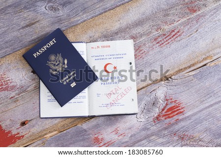 An American and Turkish passport lying on an old wooden table with the Turkish passport opened to reveal a cancelled hand stamp conceptual of immigration and changing citizenship
