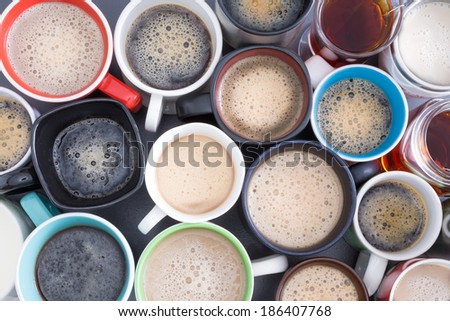 Background with a view from above of closely packed assorted mugs full of fresh hot coffee covered in froth