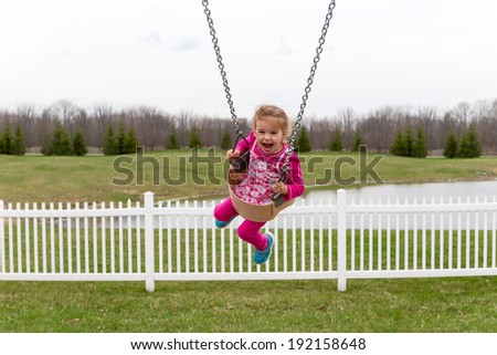 Beautiful excited little girl on a garden swing screaming in delight and laughing as she flies high in the air against a rural background