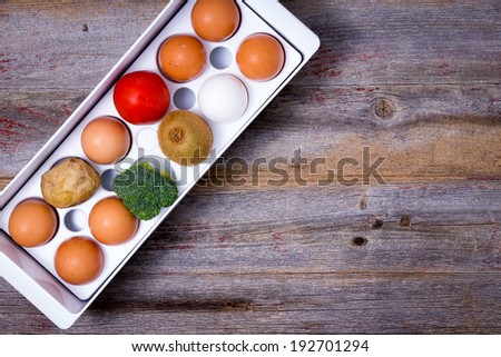 Conceptual image of storage and management of food in the refrigerator with a view from above of a plastic egg tray with eggs, broccoli, tomato, kiwifruit and a potato on a wooden table with copyspace